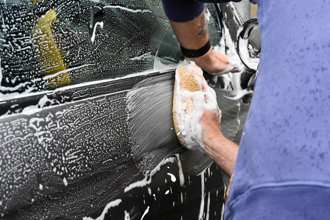 Detail technician hand-washing a car with sponge and soap suds